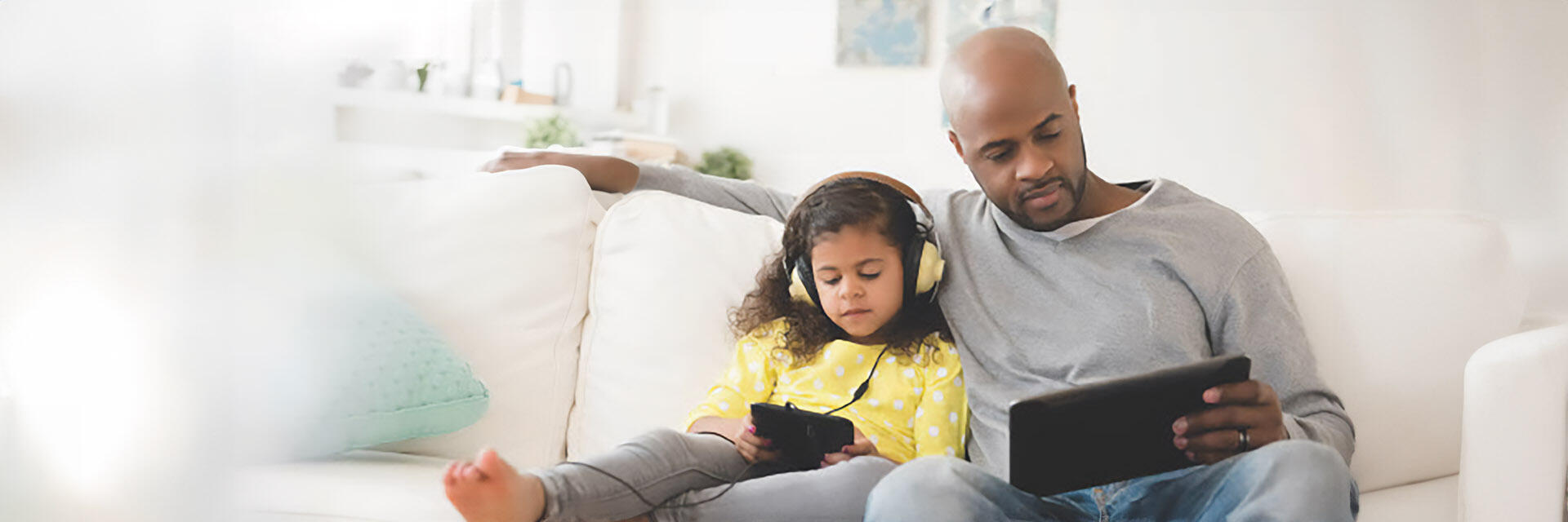 A father and daughter playing with battery powered devices on their couch.